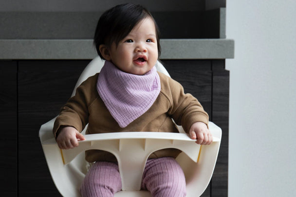Baby Kiara sitting in a highchair wearing a KIDLY Label bib, sweatshirt and leggings